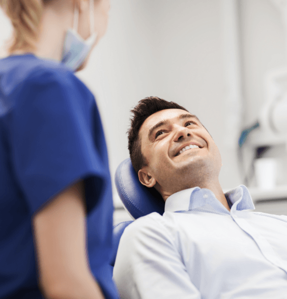 Man in a blue shirt, smiling, standing in a dental office with dental tools in the background.
