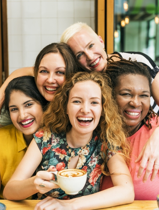 Five smiling women sitting at table in coffee shop