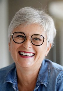 Mature woman smiling in denim shirt and black-framed glasses