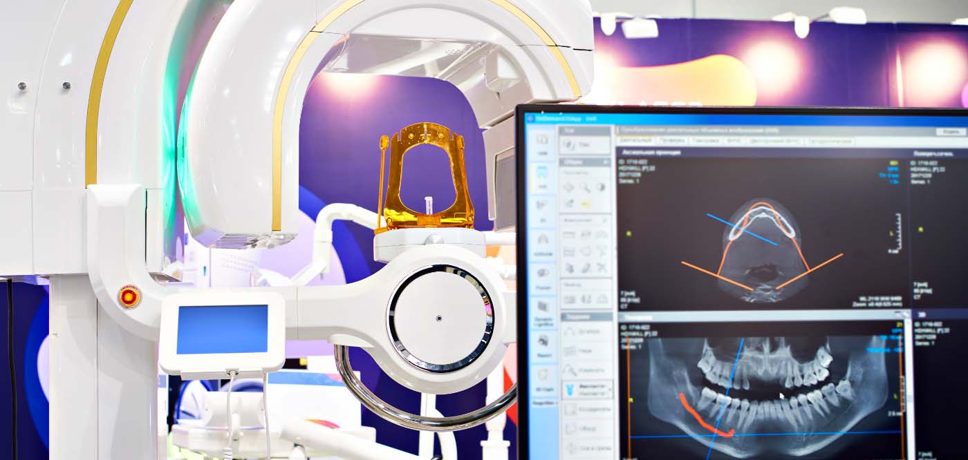Dental x ray machine with computer monitors in foreground showing 3 D models of jaws and teeth