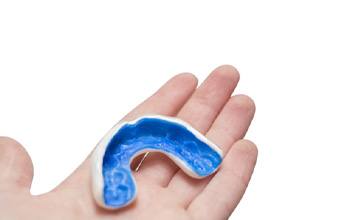 Hand holding a blue and white athletic mouthguard